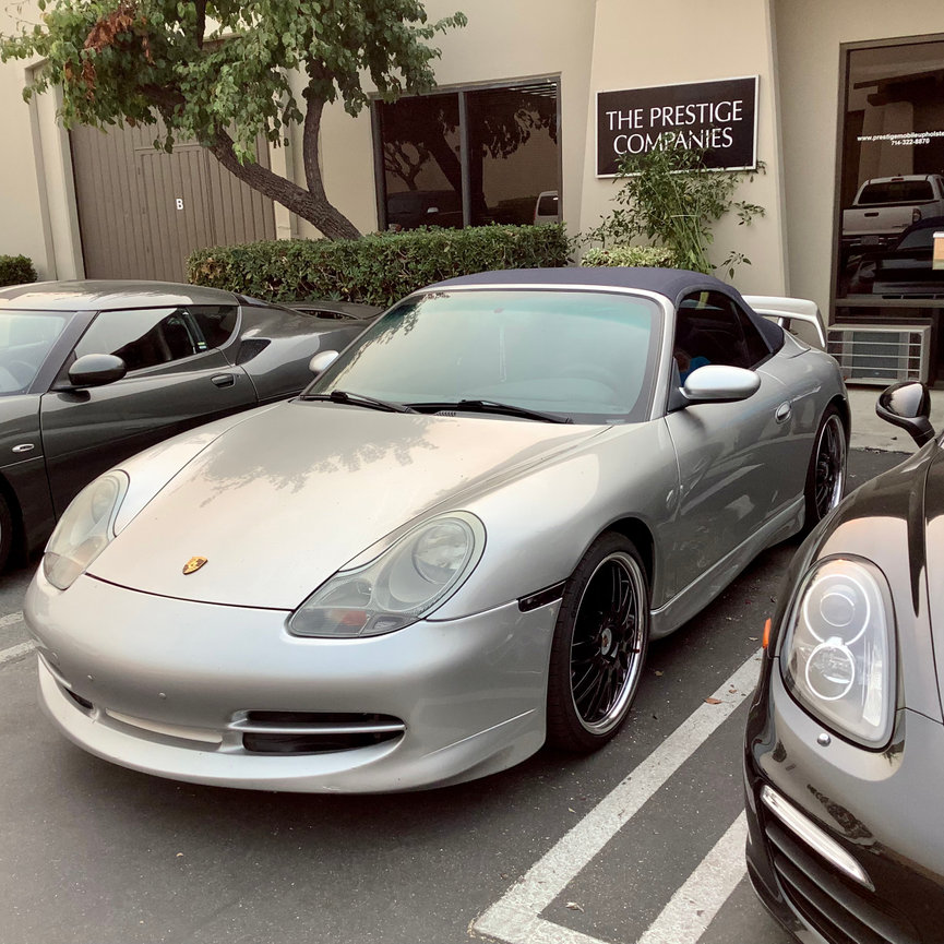 Silver Porsche with Dark Blue Convertible parked in front of The Prestige Companies Auto Upholstery.